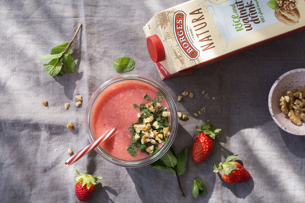 Batido de fresas sin azúcar y sin lactosa servido en un vaso con hojas de menta y trozos de nuez