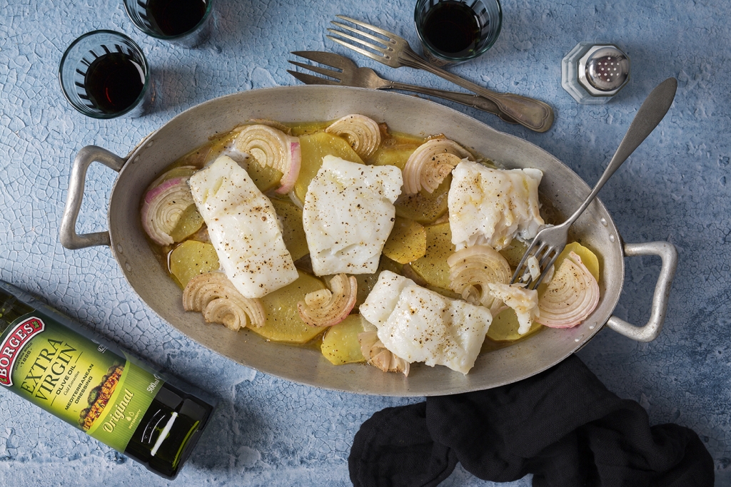 Bacalao al horno servido en una bandeja sobre base de patatas y cebolla
