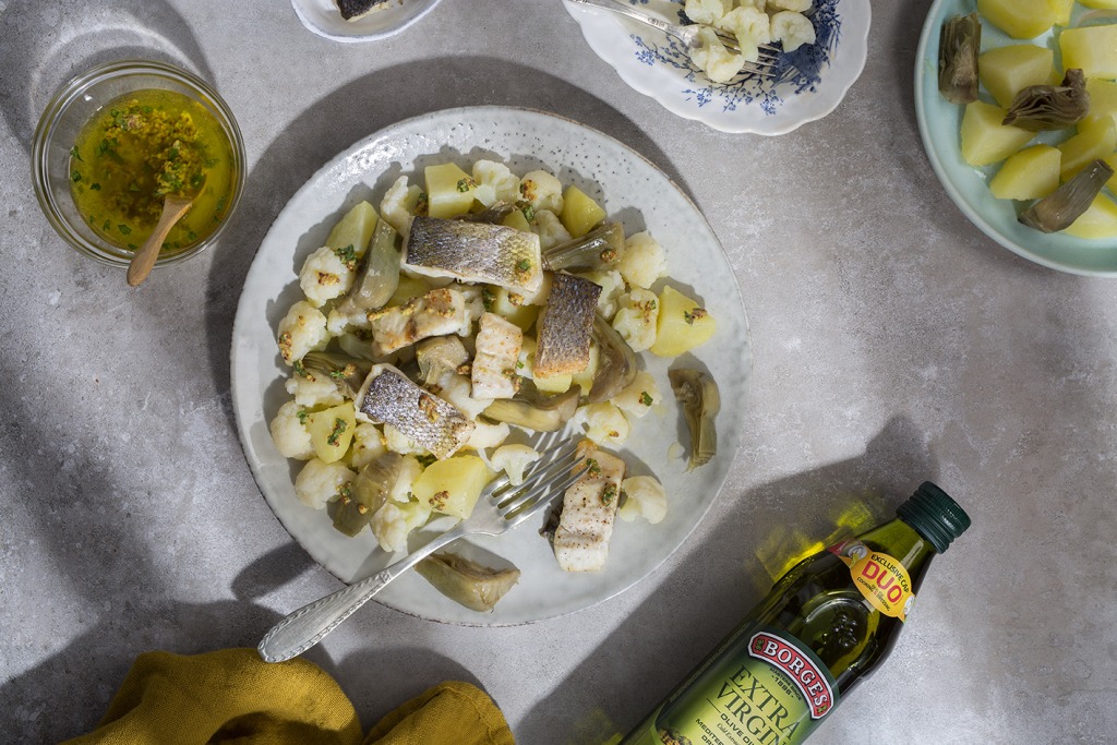 Sea bass and artichoke salad served in a white dish and seasoned with a cup of olive oil