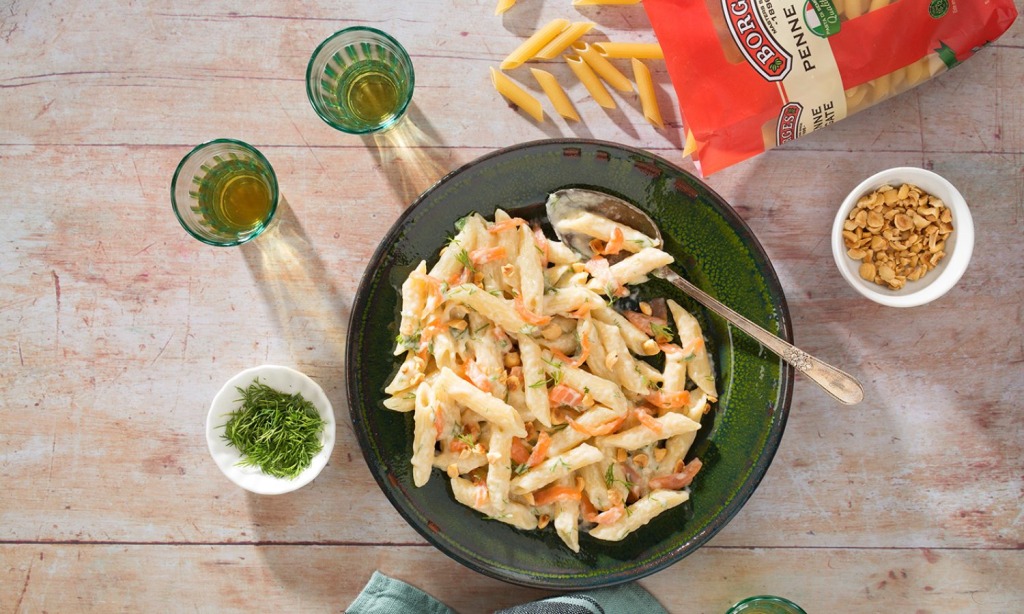 Salmon penne pasta recipe served in a green dish with nuts, herbs and olive oil